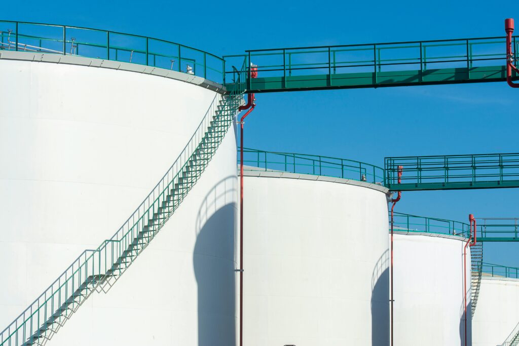 Large industrial storage tanks with a green walkway under a clear blue sky.